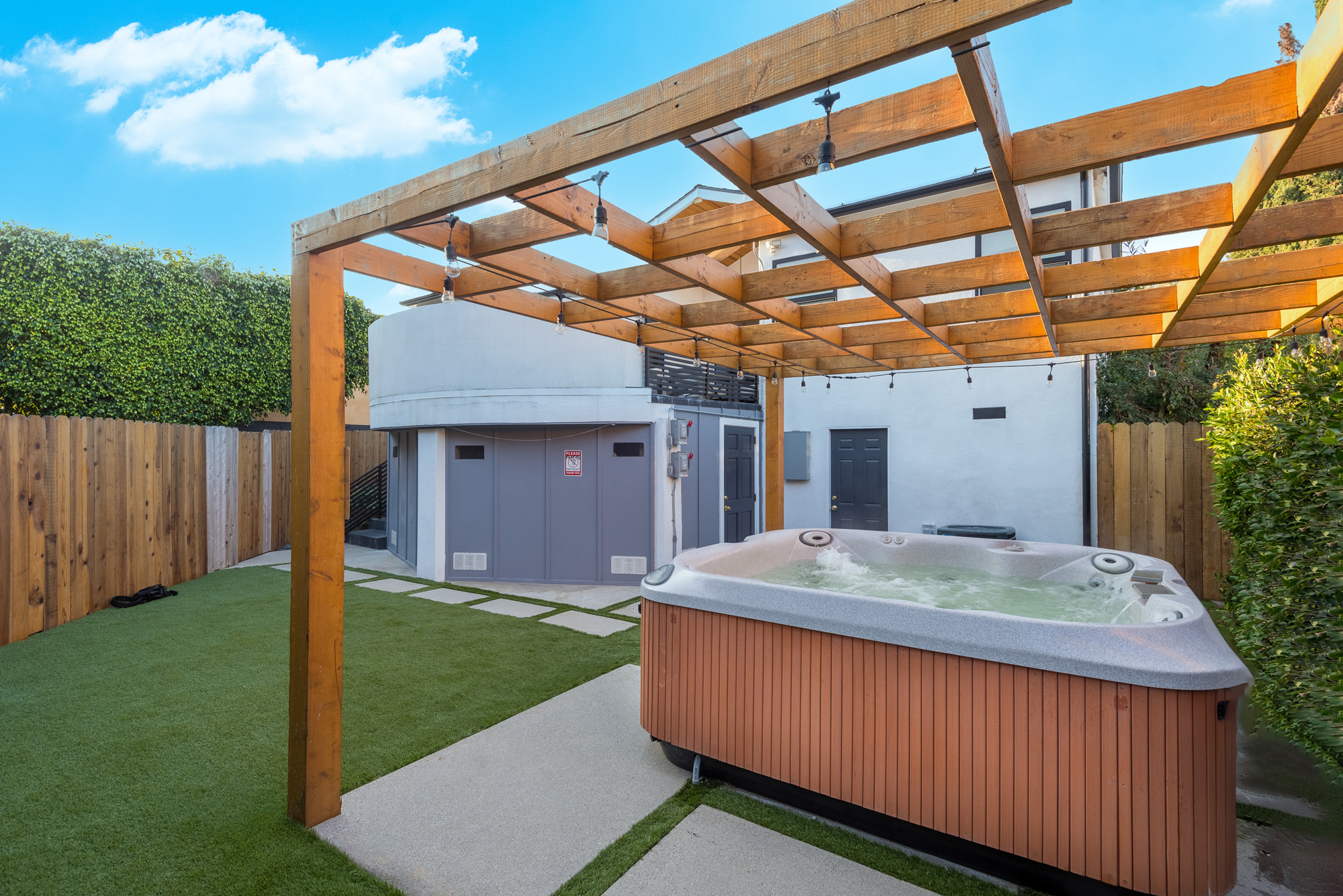 Pergola over a hot tub with paver path and lawn