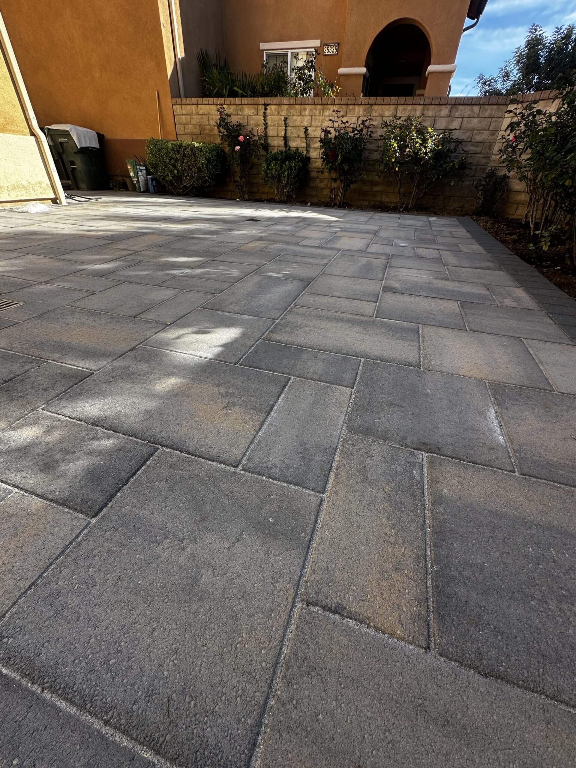 Paver patio bordered by rose beds and brick wall