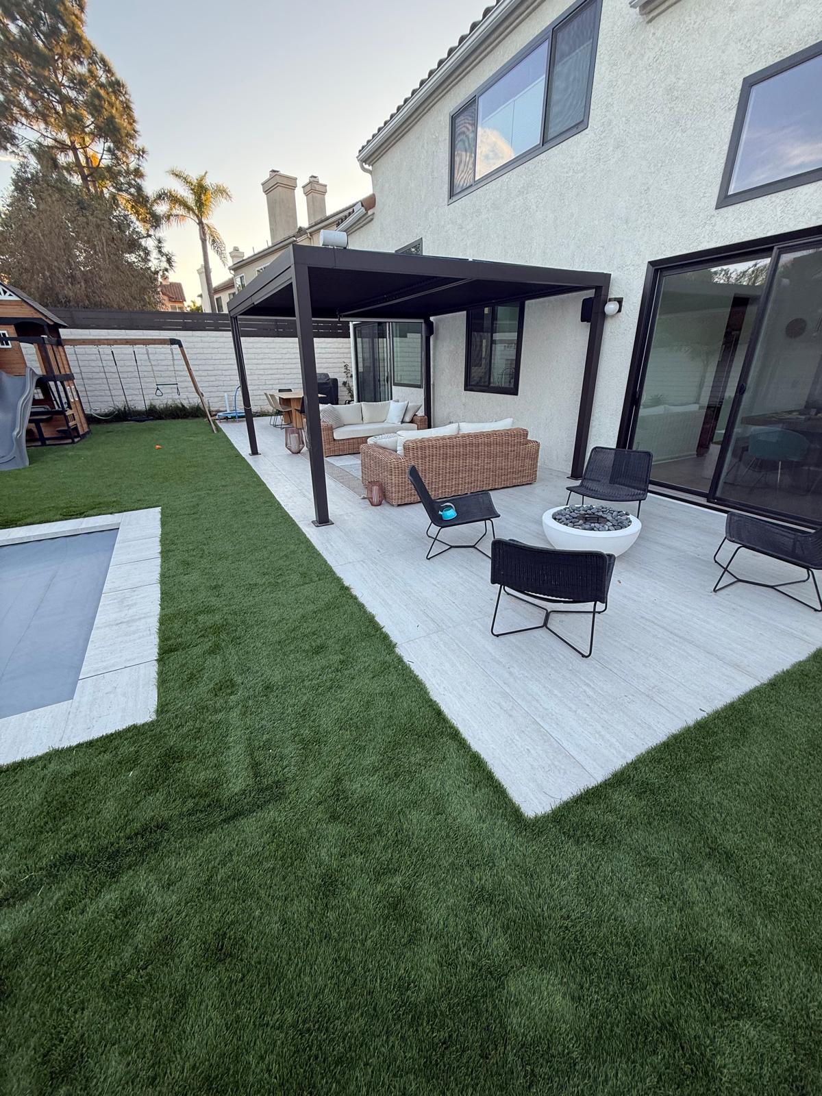 Covered patio lounge with fire pit beside a turf lawn