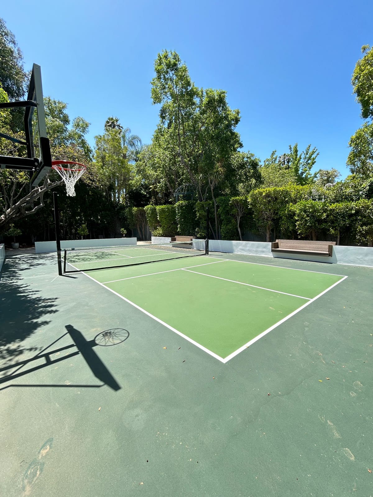 Green sport court with bench seating shaded by trees