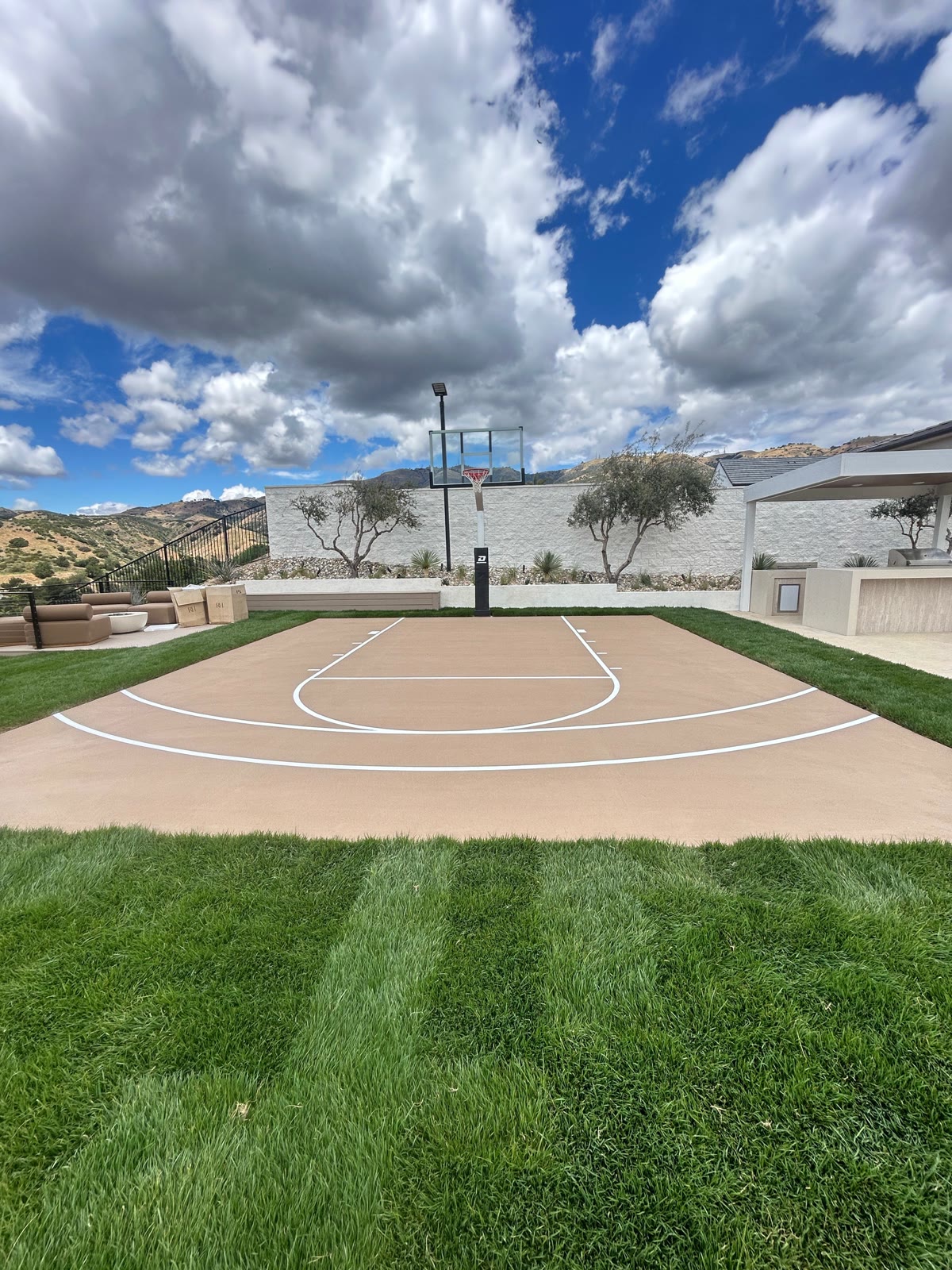 Tan court and green lawn under big sky with mountain views