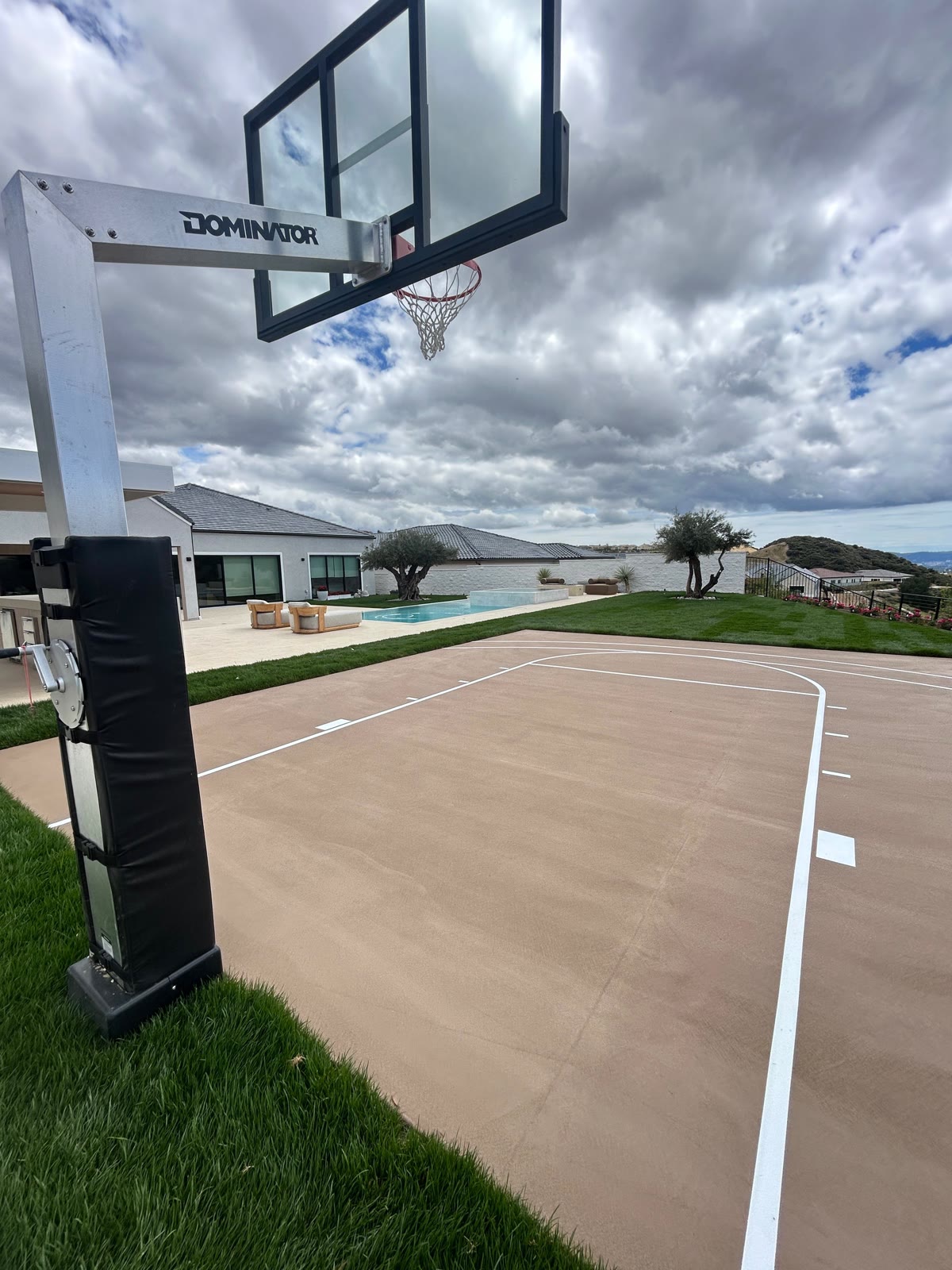 Backyard basketball court with pool and lake view under dramatic clouds