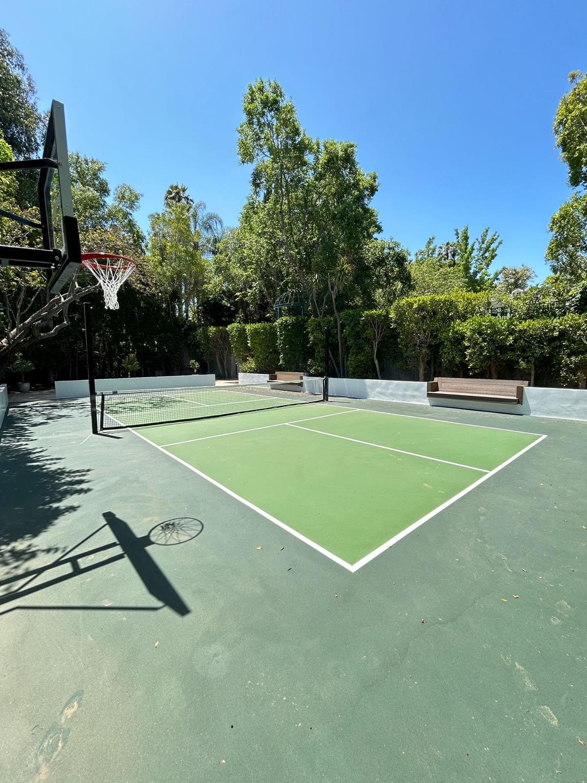 Green sport court framed by lush trees and a basketball hoop