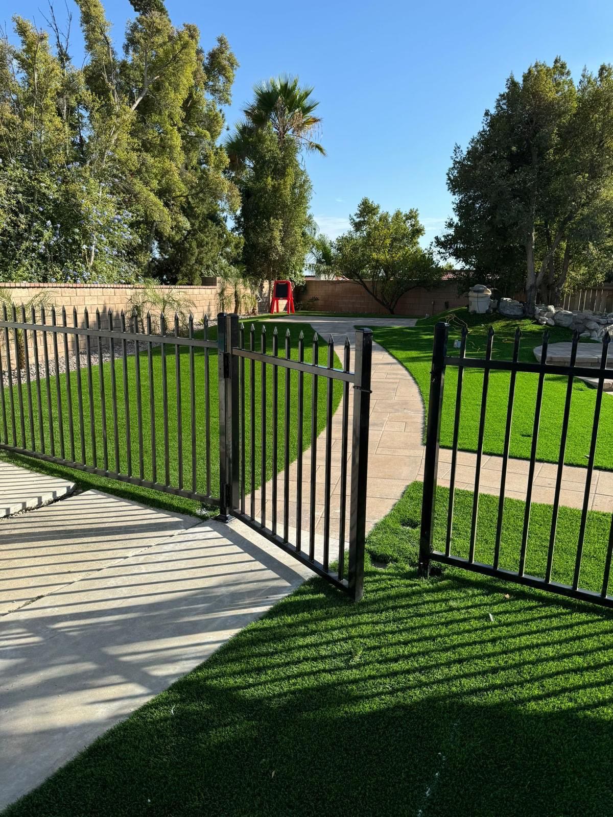 Black metal tubular gate opening to a lush green lawn