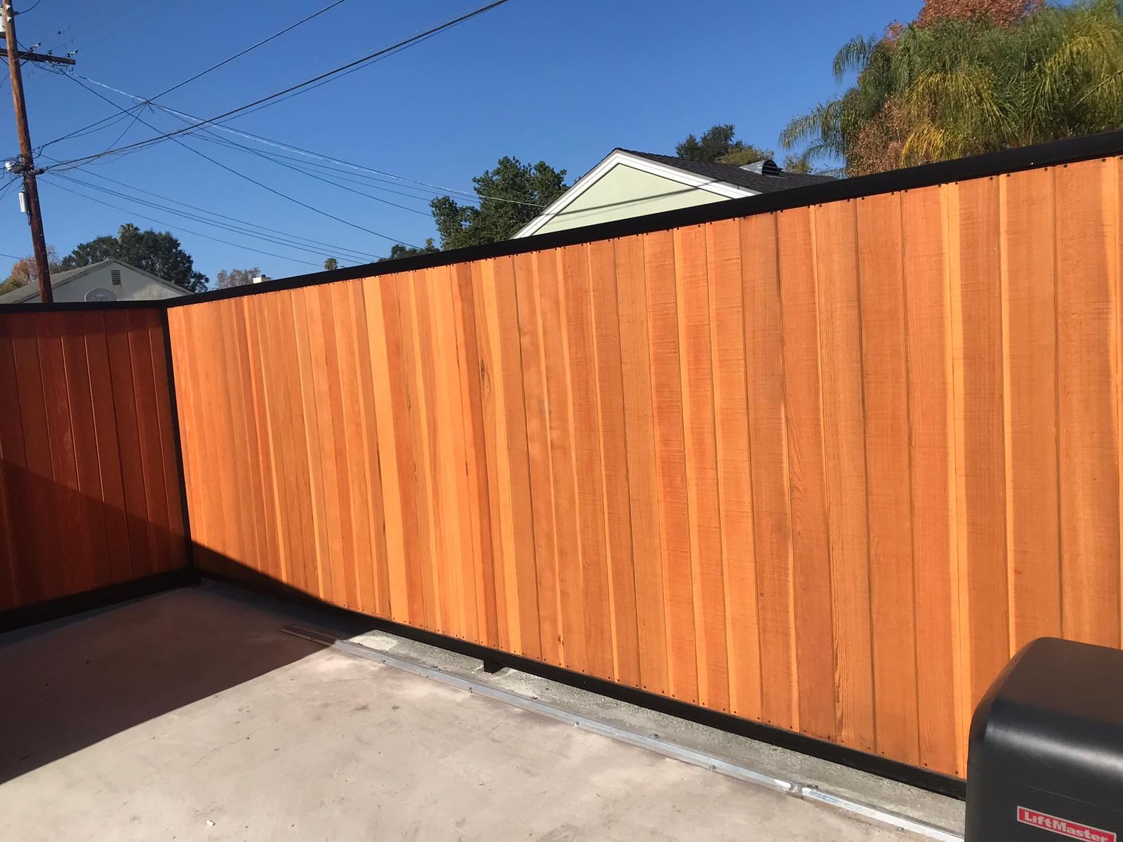 Warm cedar privacy fence with black-frame sliding gate under blue sky