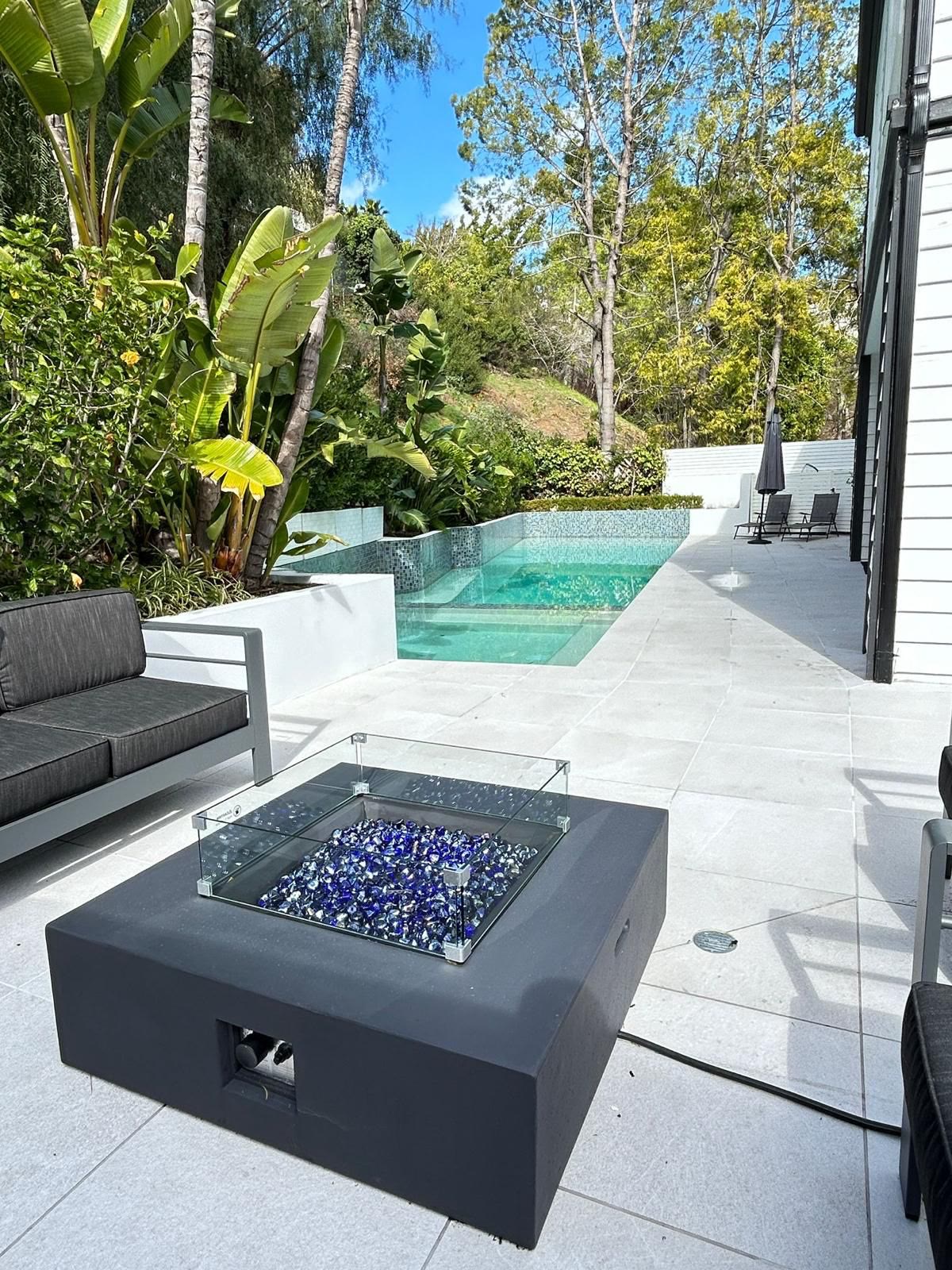 Modern fire-glass pit table with lounge seating beside the pool