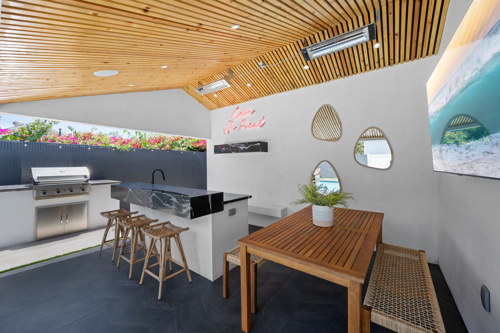 Covered outdoor kitchen with built-in grill, marble bar island, and dining table