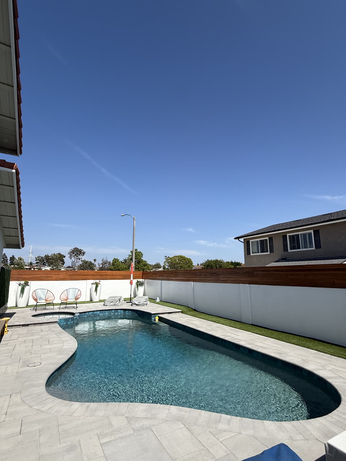 Freeform pool with paver deck and modern wood fence