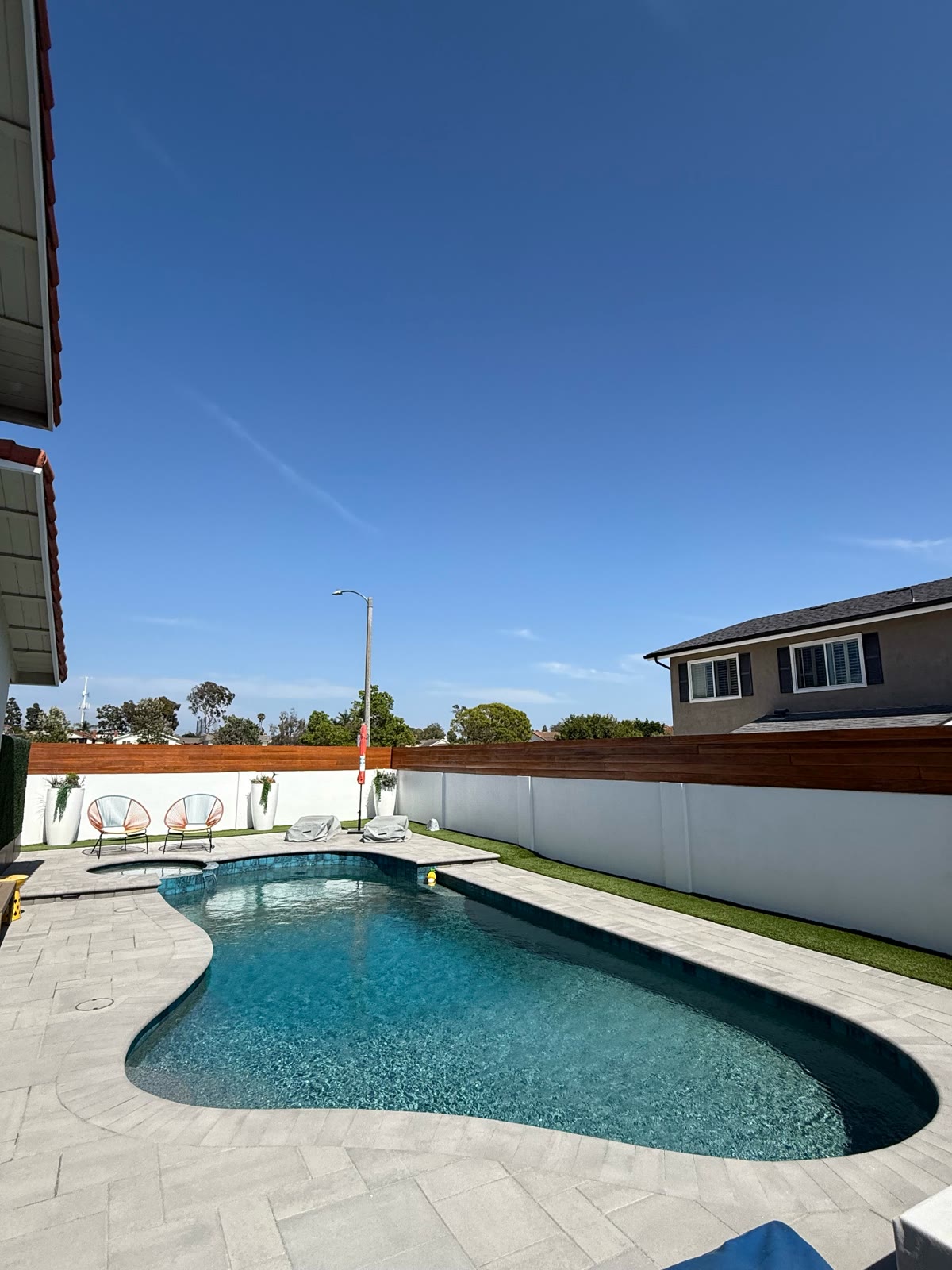 Freeform pool and spa with paver deck and modern wood fence