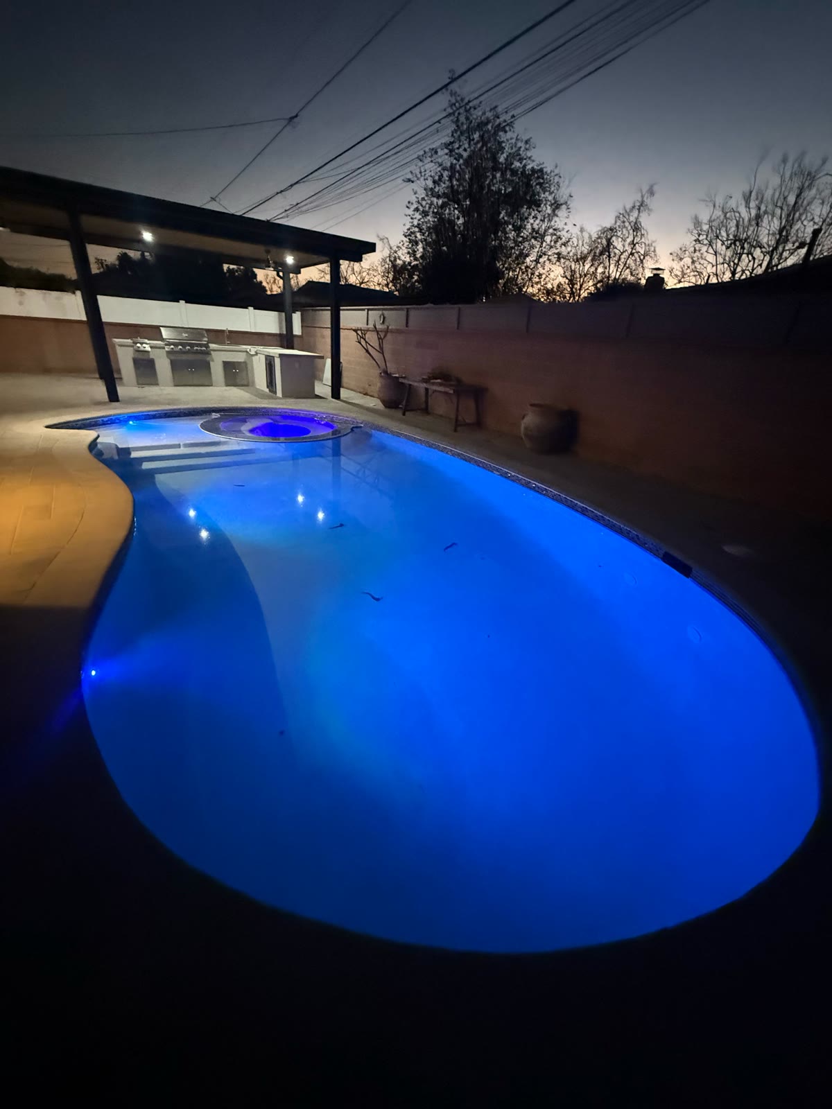 Pool lit blue at dusk with outdoor kitchen and patio cover