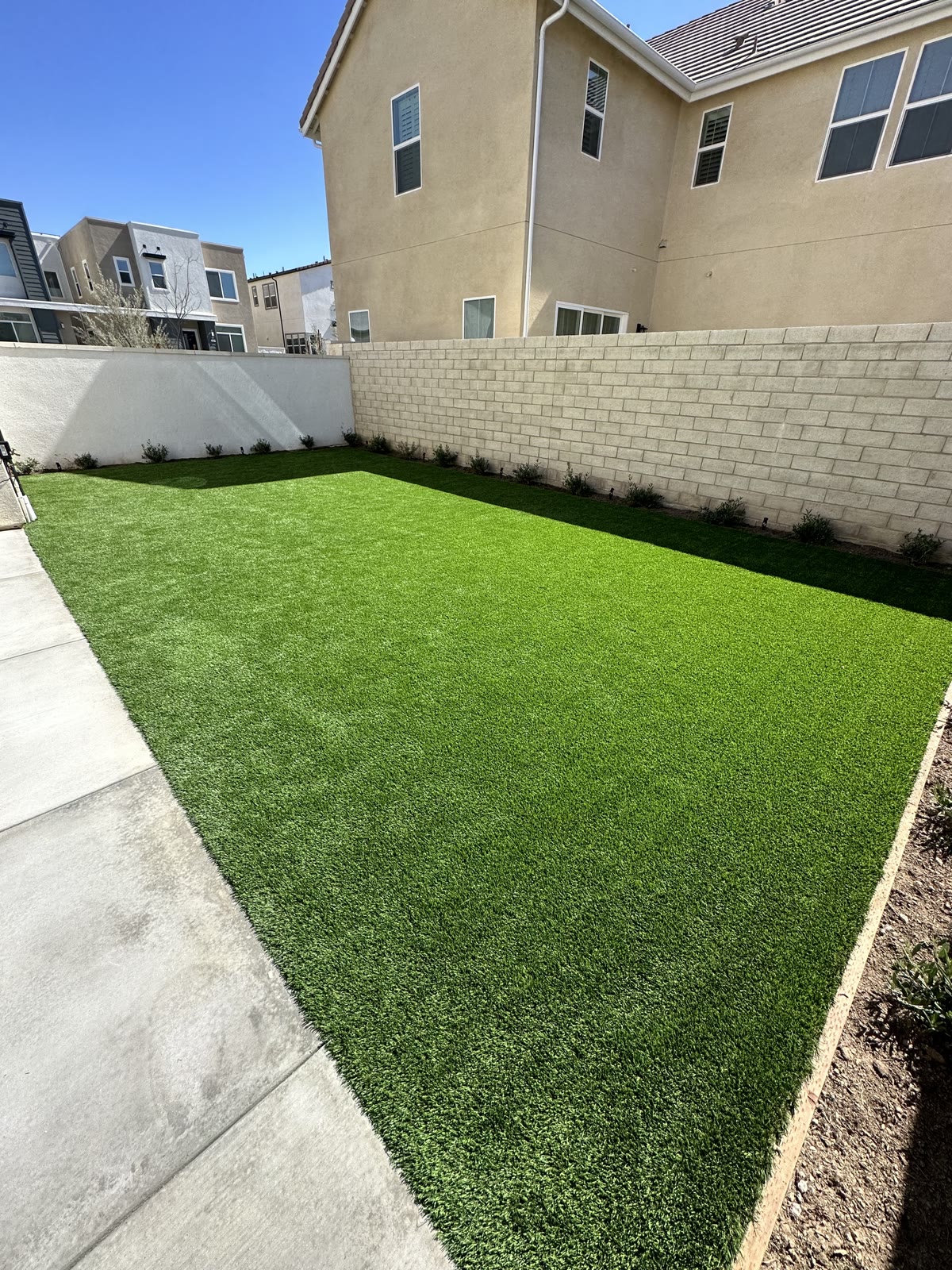 Fresh artificial turf lawn beside a block wall and home