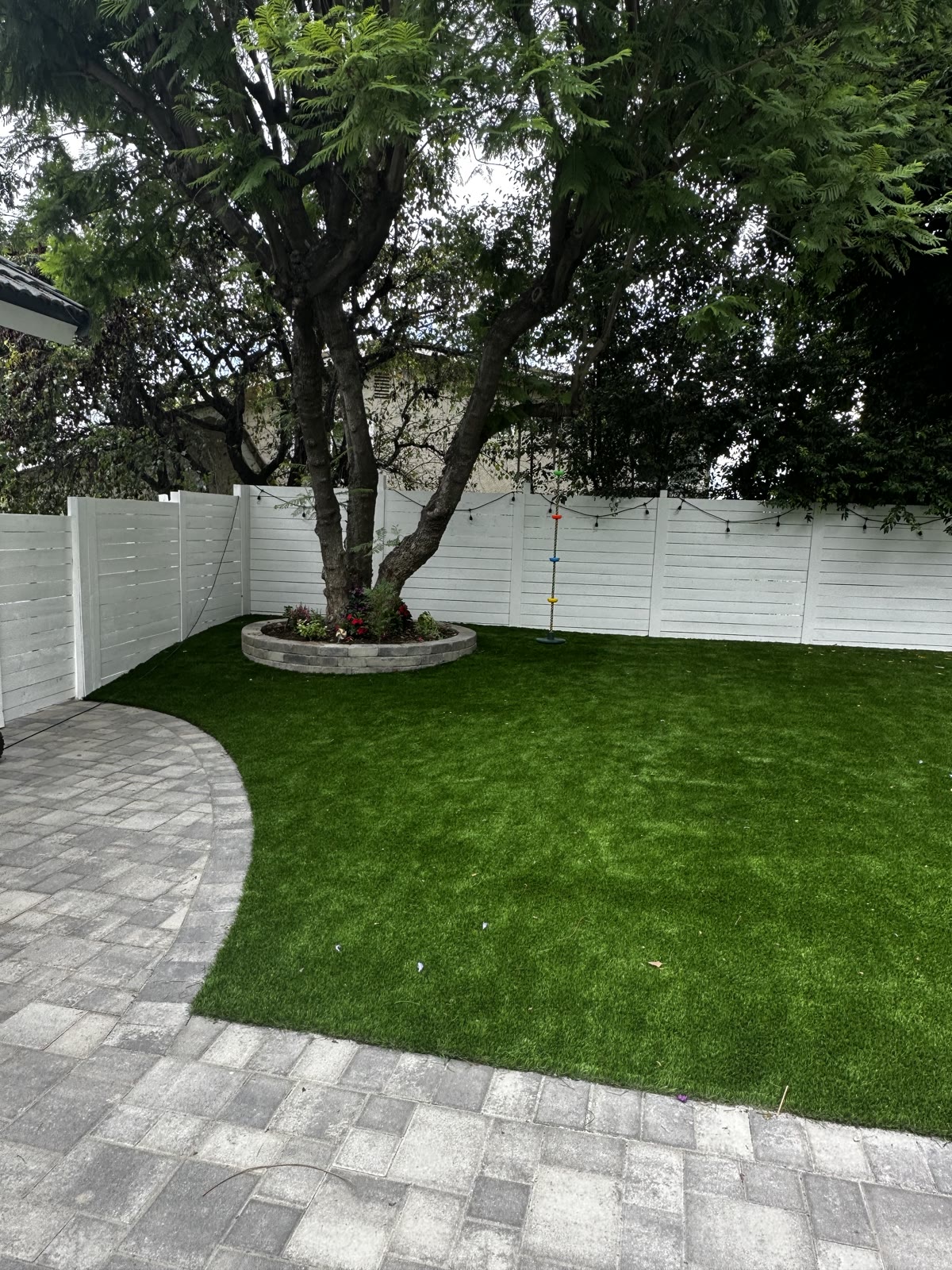 Turf lawn wrapping a mature tree in a paver planter